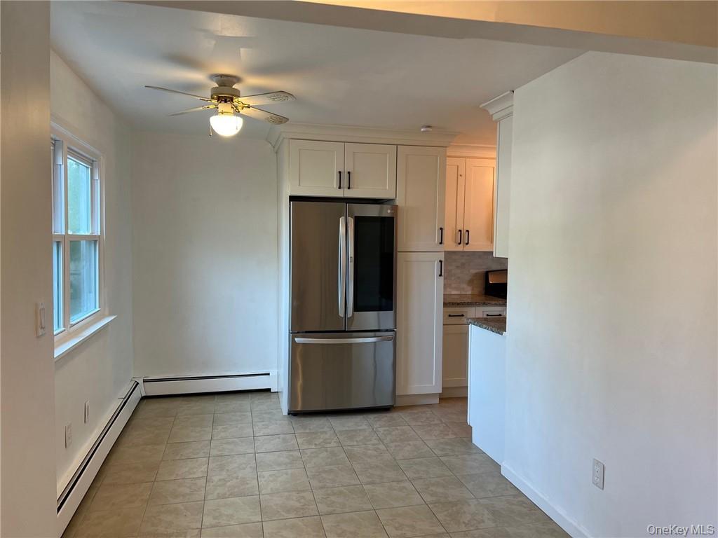 38 Hampton Court Middletown, NY 10941 - Photo 2 of 17 Kitchen and small dining area with a baseboard heating, ceiling fan, stainless steel refrigerator, and white cabinets
