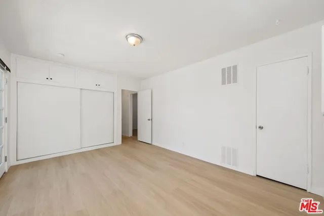 a view of an empty room with wooden floor and closet