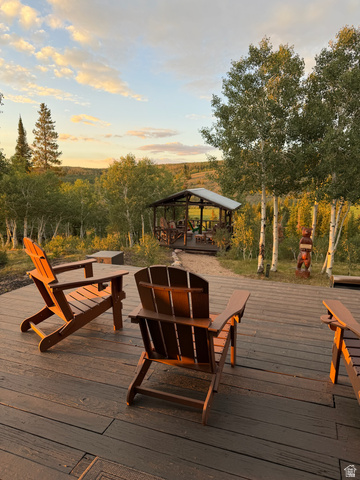 1663 Lancer Lane Evanston, UT 82930 - Photo 33 of 101 Expansive outdoor deck featuring composite decking and a built-in wooden gazebo with a metal roof, surrounded by mature trees and natural landscaping