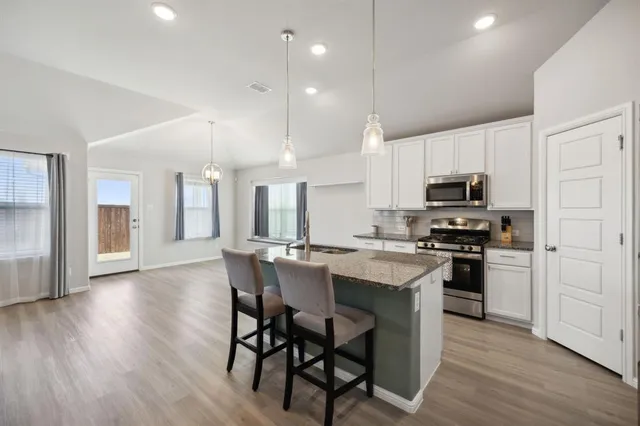 a kitchen with stainless steel appliances granite countertop a stove top oven a sink dishwasher a refrigerator and white cabinets with wooden floor