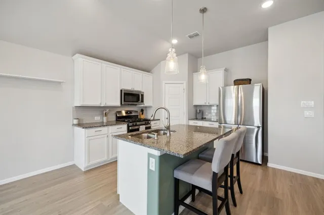 a kitchen with stainless steel appliances granite countertop a stove top oven a refrigerator a sink and a dining table with wooden floor