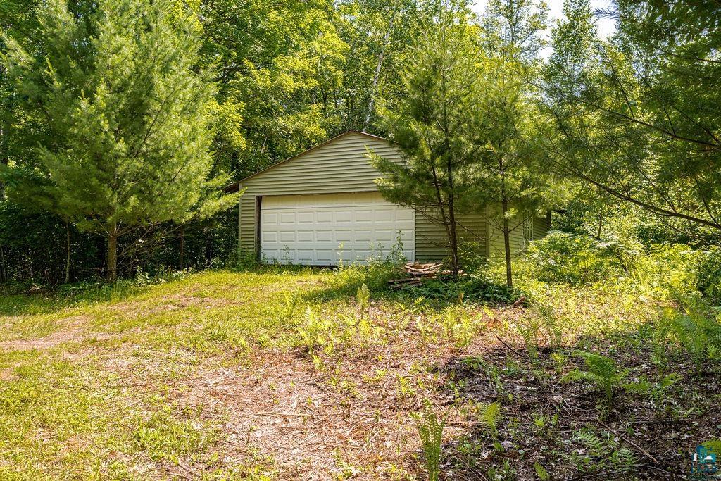 2592 Strandberg Road Barnum, MN 55707 - Photo 29 of 44 Detached garage with horizontal siding and a white panel garage door, surrounded by mature trees and natural landscaping