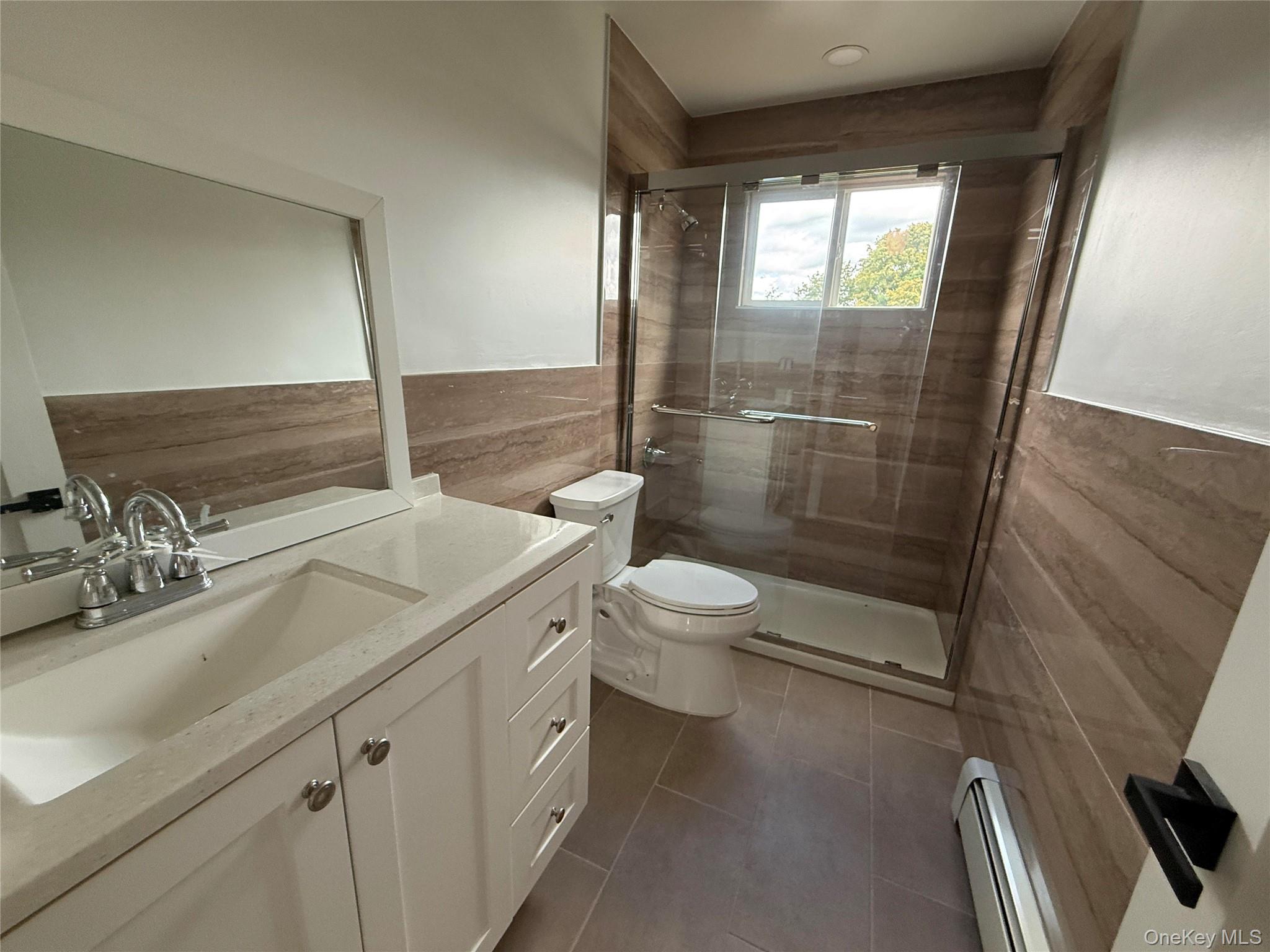324 Buckingham Road Cedarhurst, NY 11516 - Photo 8 of 12 Full bathroom featuring tile walls, vanity, a baseboard heating unit, a shower stall, and dark tile patterned floors