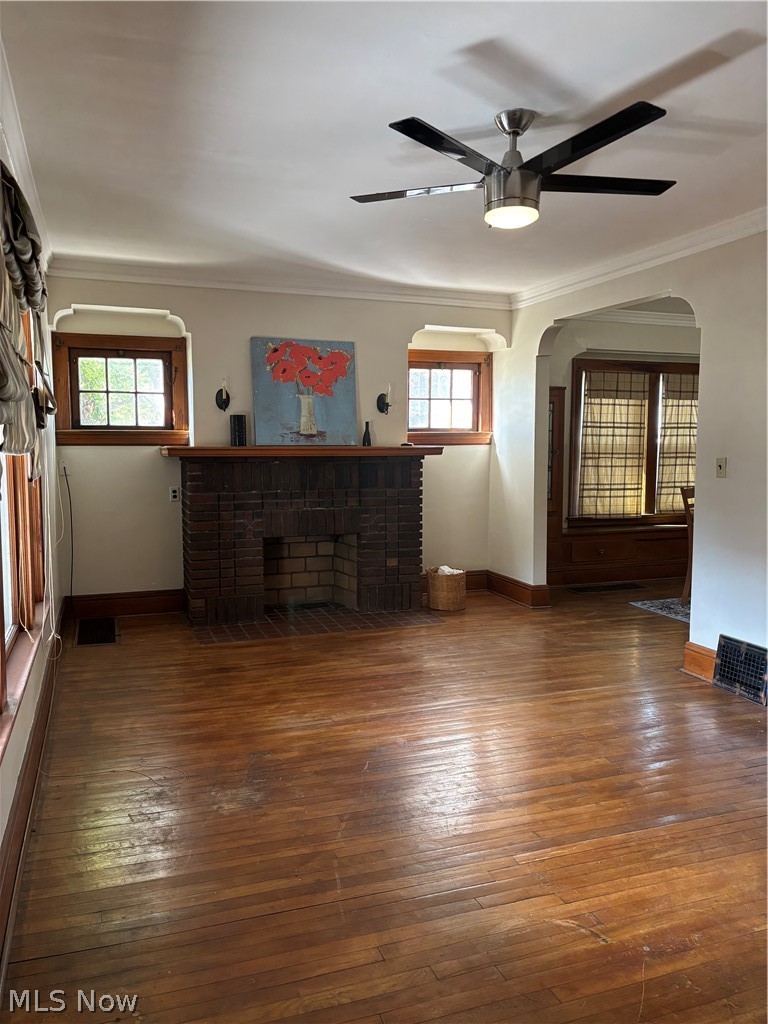Brick fireplace with a wood mantel, wood-finish flooring, and a contemporary ceiling fan with integrated lighting