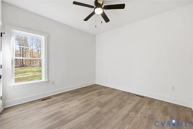 a view of empty room with wooden floor and fan