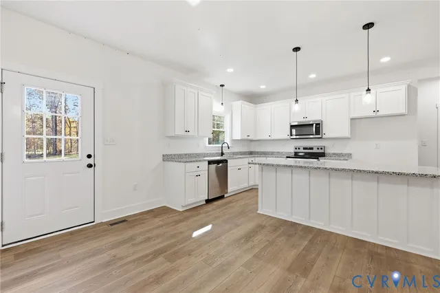 a kitchen with stainless steel appliances kitchen island granite countertop a stove a sink and white cabinets with wooden floor