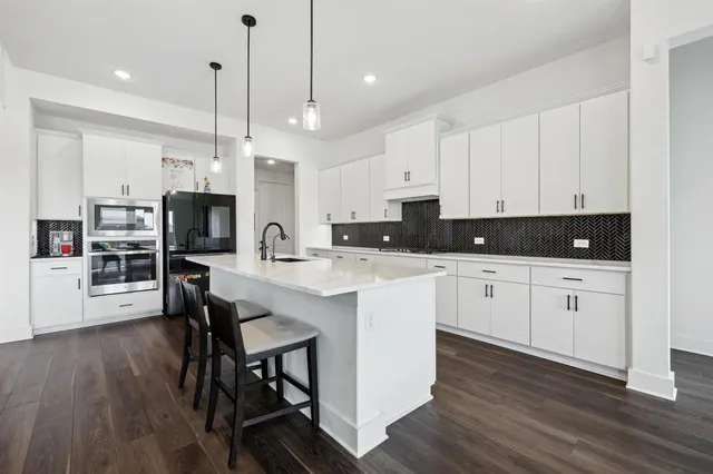 a kitchen with stainless steel appliances kitchen island granite countertop a refrigerator a stove a sink a dining table and chairs with wooden floor