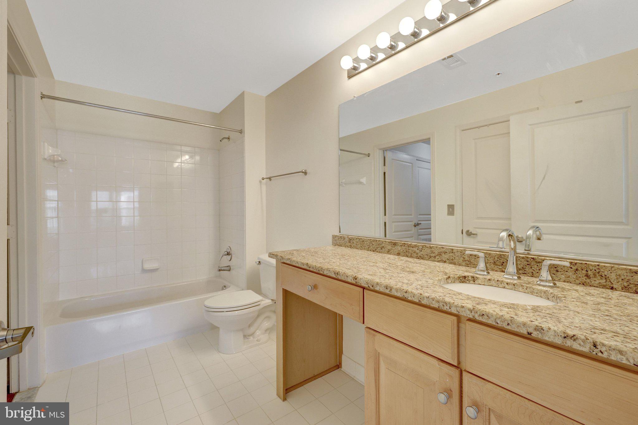 12001 Market Street, Unit 434 Reston, VA 20190 - Photo 25 of 43 a bathroom with a granite countertop sink a toilet a shower and a mirror