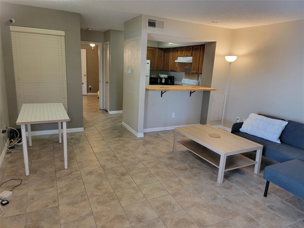 9803 Walnut Street, Unit 102 Dallas, TX 75243 - Photo 5 of 17 Spacious living area featuring neutral-toned tile flooring, light gray wall paint, and a breakfast bar with a light wood-finish countertop