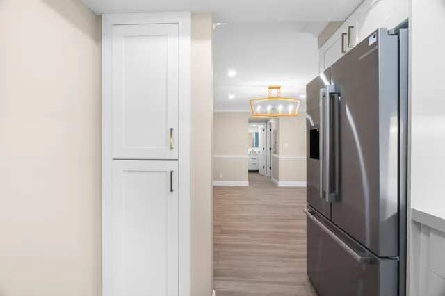 a view of a refrigerator in kitchen and an empty room with wooden floor