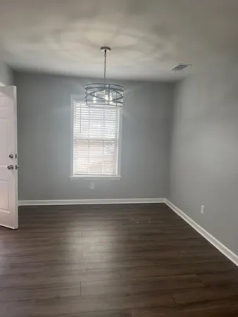 a view of an empty room with wooden floor fridge and a window