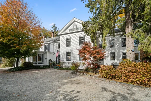 a view of a white house next to a yard with large trees