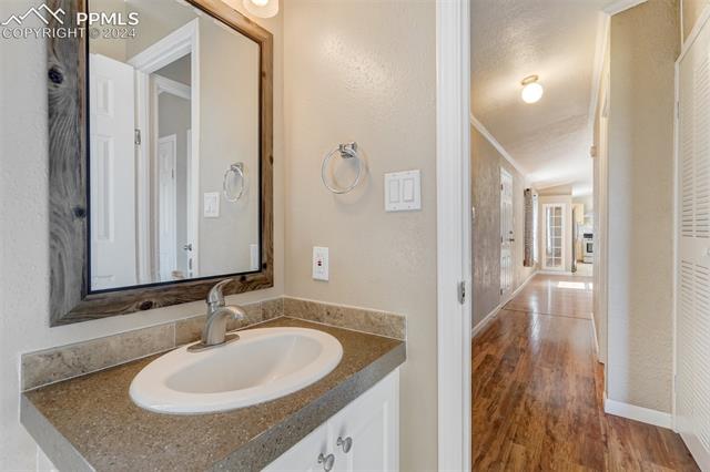 6240 Night Train Lane Yoder, CO 80864 - Photo 38 of 50 Bathroom featuring vanity with extensive cabinet space, hardwood / wood-style flooring, a textured ceiling, and crown molding