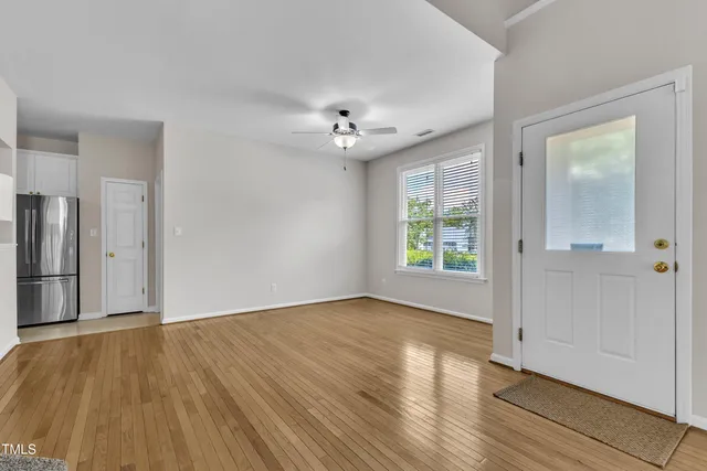 an empty room with wooden floor chandelier fan and windows