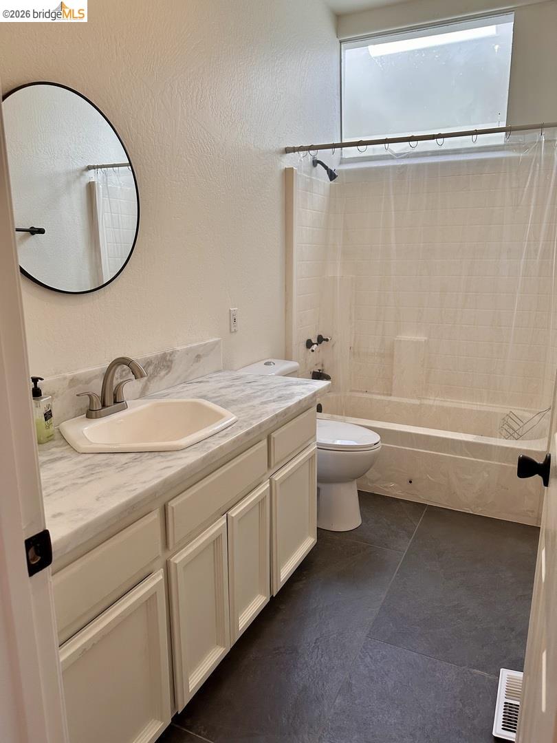 2080 Nelson Road Camino, CA 95709 - Photo 46 of 55 Vanity with white shaker-style cabinetry and a light-toned countertop, undermount sink with a brushed nickel faucet, large round wall mirror, bath with a shower and subway tile surround, and dark-toned floor tiles