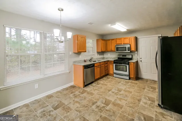 a kitchen with stainless steel appliances granite countertop a stove top oven a sink dishwasher a refrigerator and white cabinets with wooden floor
