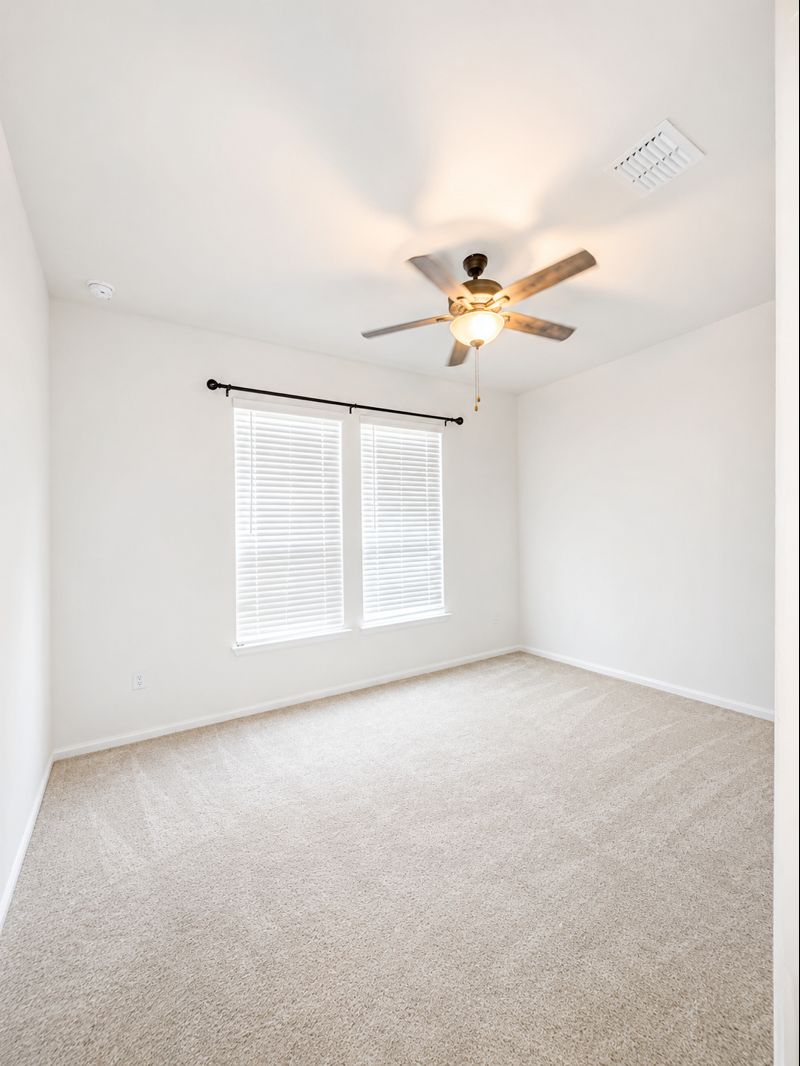 693 Durian Loop Buda, TX 78610 - Photo 5 of 27 An inviting room with plush carpeting and a ceiling fan, offering a comfortable personal retreat.