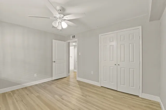 a view of an empty room with wooden floor and a ceiling fan