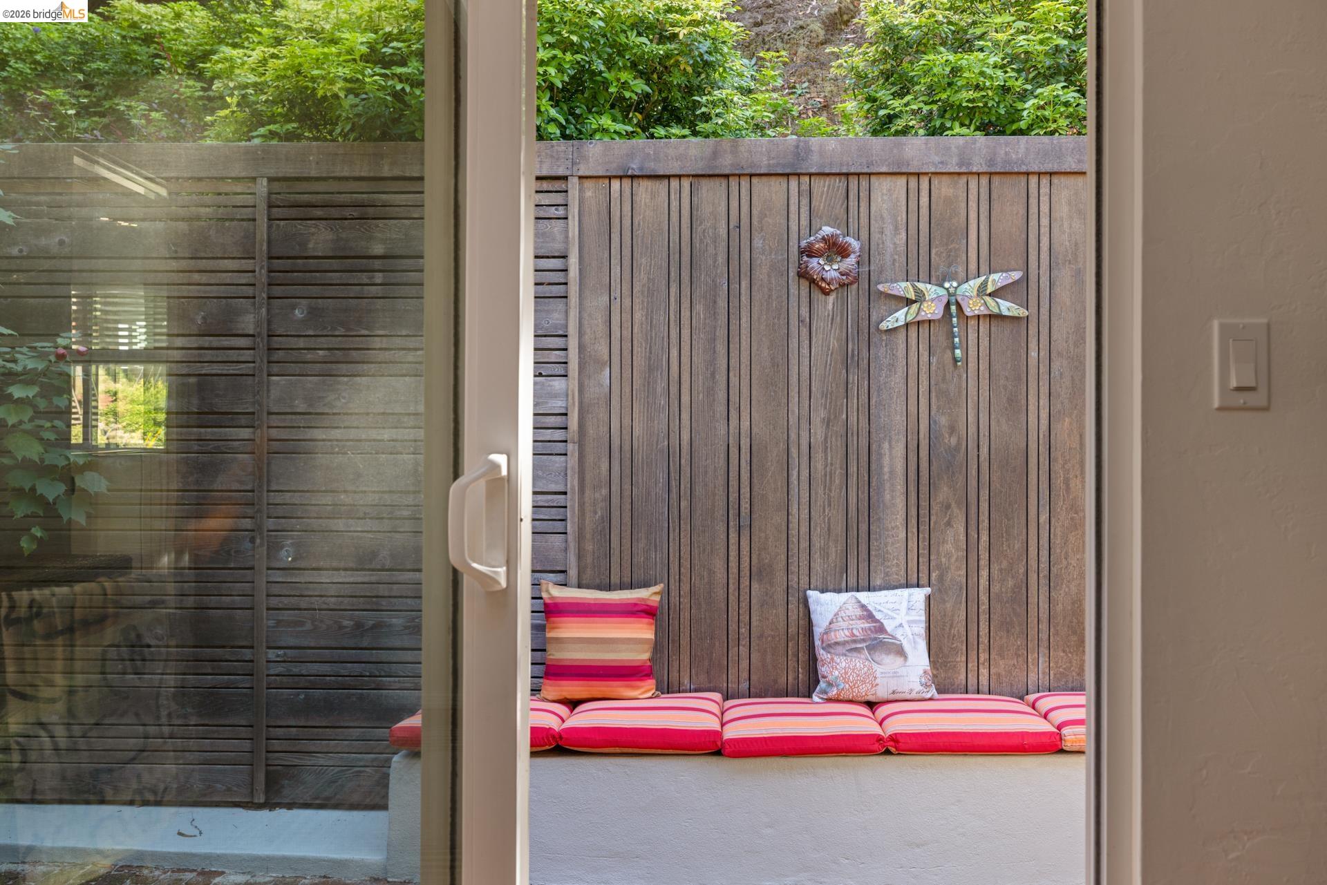 6660 Sobrante Road Oakland, CA 94611 - Photo 34 of 48 Sliding glass patio door opening to a private outdoor space with a wood-paneled wall, built-in bench seating, and surrounding greenery