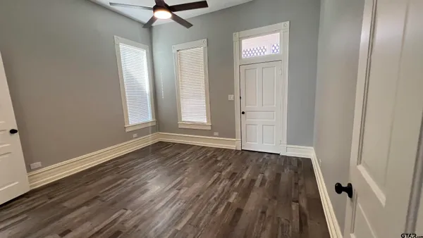 an empty room with wooden floor fan and windows