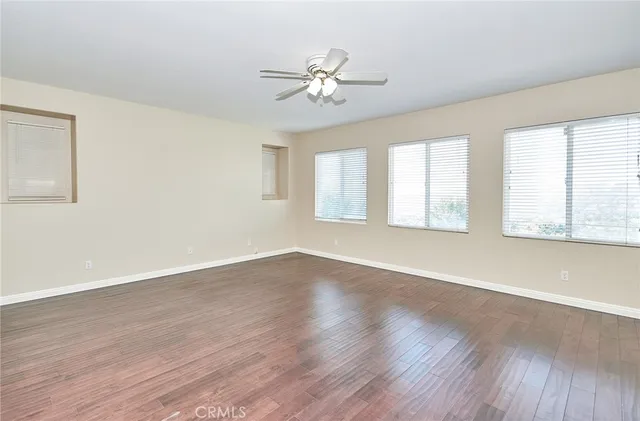 an empty room with wooden floor fan and windows