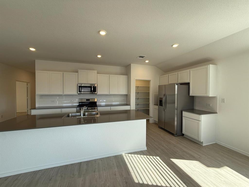 263 Magalia Lane Kyle, TX 78640 - Photo 17 of 37 a large kitchen with stainless steel appliances kitchen island a sink dishwasher a refrigerator and white cabinets with wooden floor