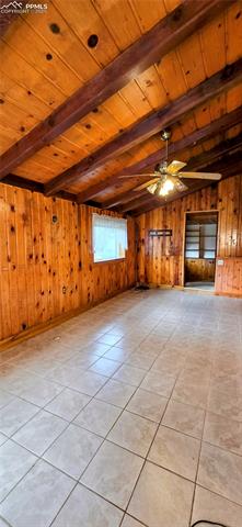 11785 Milam Road Colorado Springs, CO 80908 - Photo 17 of 44 Unfurnished living room with light tile patterned flooring, a wood ceiling with exposed beams, wooden walls, and ceiling fan