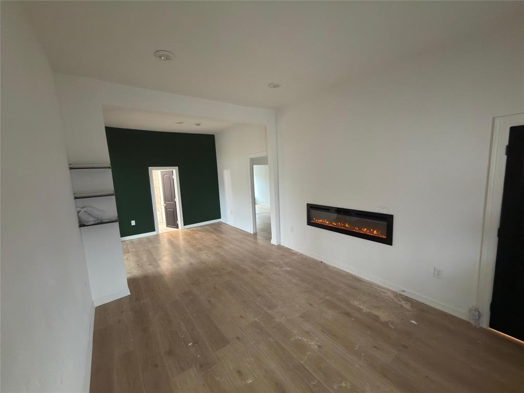 216 West 9th Street Bonham, TX 75418 - Photo 3 of 9 Unfurnished living room with a glass covered fireplace and wood finished floors