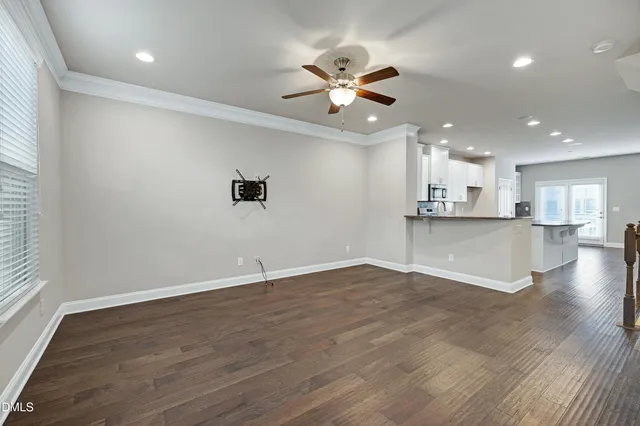 an empty room with wooden floor a ceiling fan a kitchen view and a window