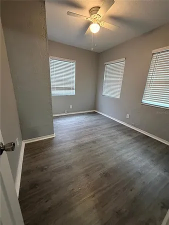 an empty room with wooden floor fan and windows