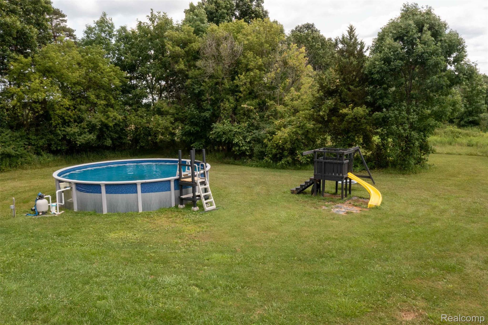 5761 Genesee Road Lapeer, MI 48446 - Photo 39 of 52 Expansive outdoor space featuring an above-ground pool with ladder access and a separate playset with slide and stairs