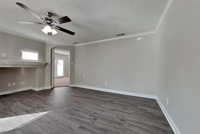 a view of an empty room with wooden floor and a ceiling fan