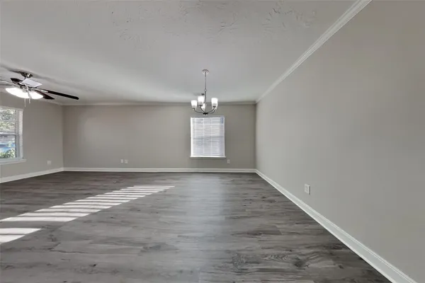 an empty room with wooden floor chandelier and windows