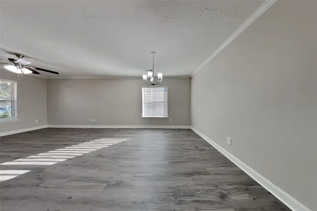 an empty room with wooden floor chandelier and windows