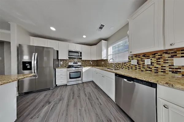 a kitchen with granite countertop a refrigerator a sink dishwasher a stove and white cabinets with wooden floor