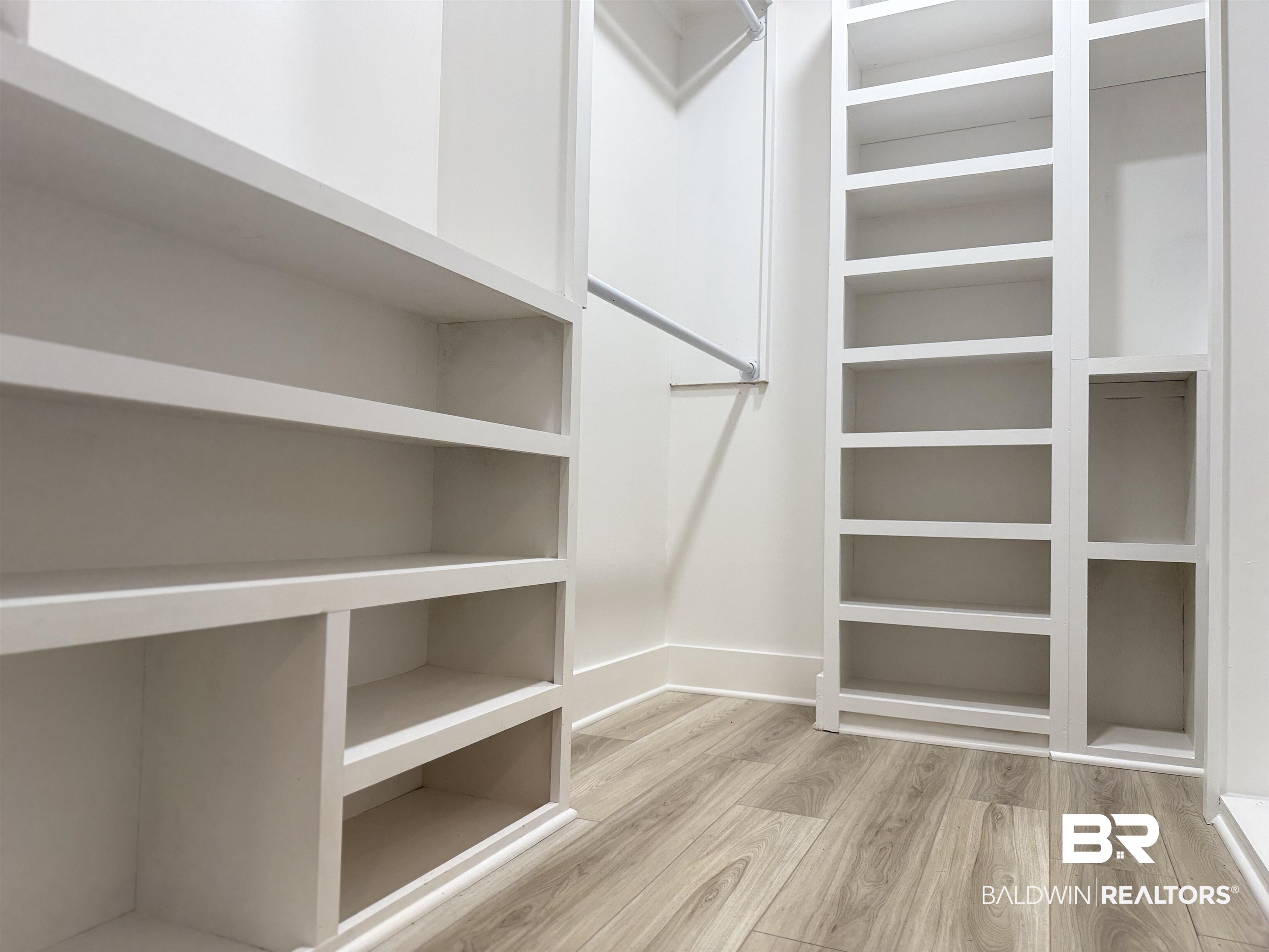 520 Juniper Place Drive Foley, AL 36535 - Photo 17 of 35 Custom walk-in closet featuring built-in white shelving, multiple hanging rods, and wood-finish flooring