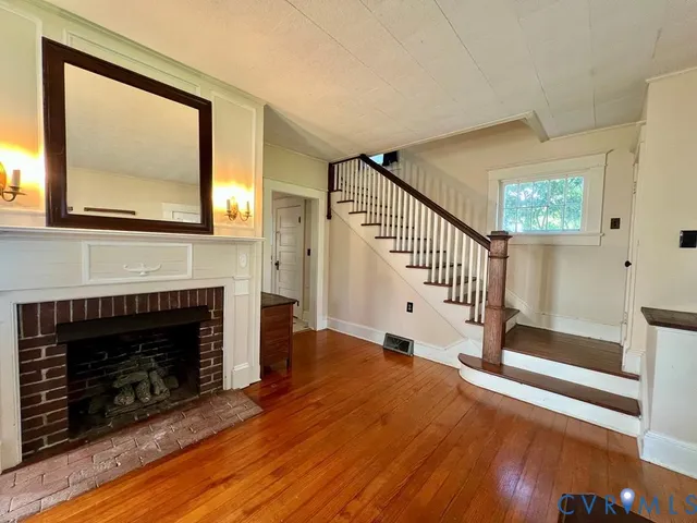 a view of an empty room with wooden floor fireplace and a window