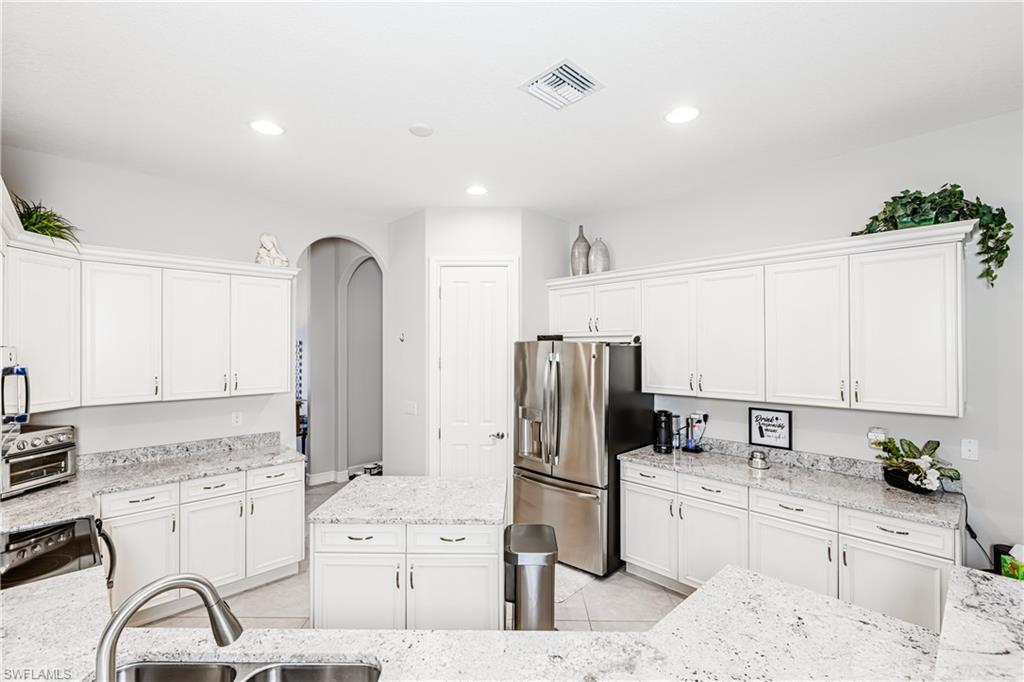 7307 Acorn Way Naples, FL 34119 - Photo 4 of 22 Kitchen featuring arched walkways, white cabinetry, stainless steel appliances, a kitchen island, and light tile patterned floors