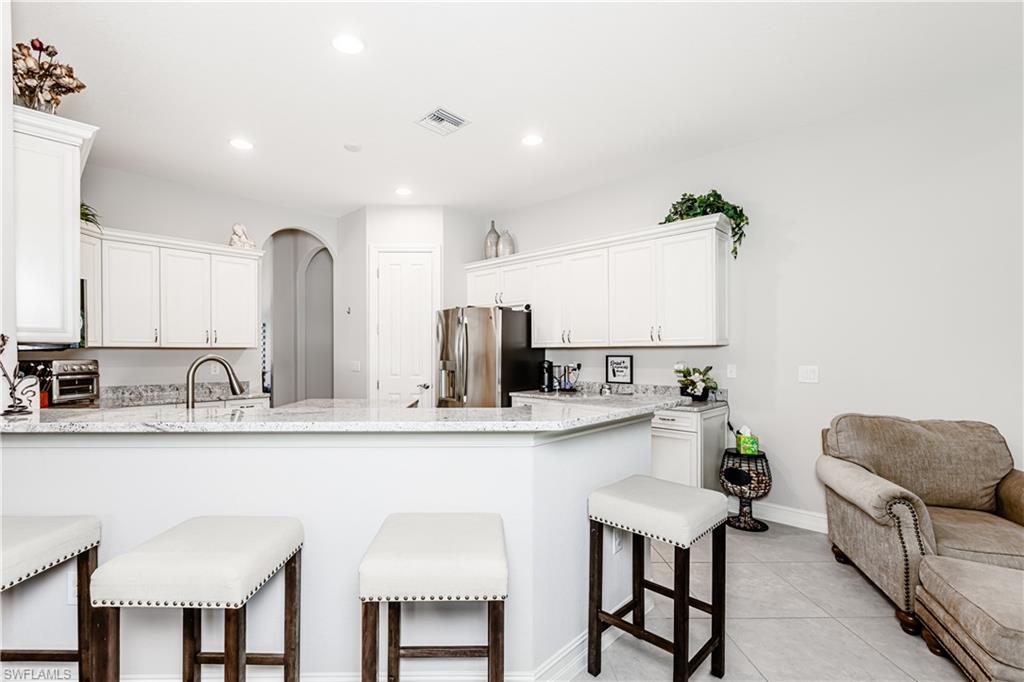 7307 Acorn Way Naples, FL 34119 - Photo 5 of 22 Kitchen with a kitchen bar, light stone countertops, white cabinetry, arched walkways, and a peninsula