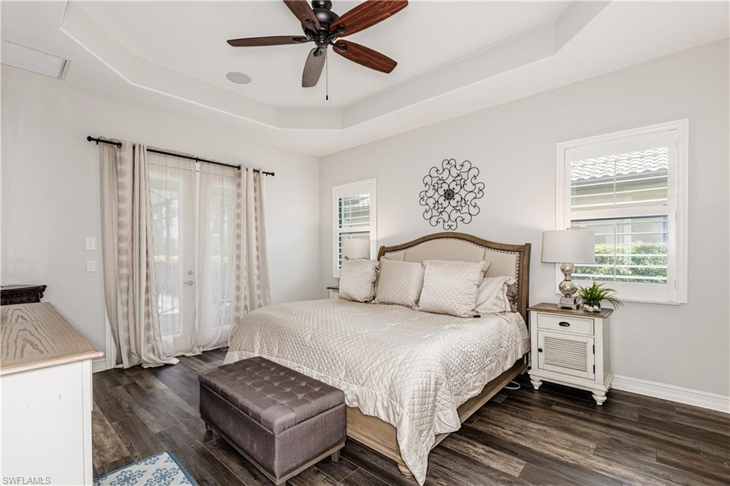 7307 Acorn Way Naples, FL 34119 - Photo 9 of 22 Bedroom featuring a tray ceiling, access to exterior, multiple windows, and dark wood-style flooring