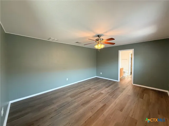 an empty room with wooden floor chandelier fan and windows