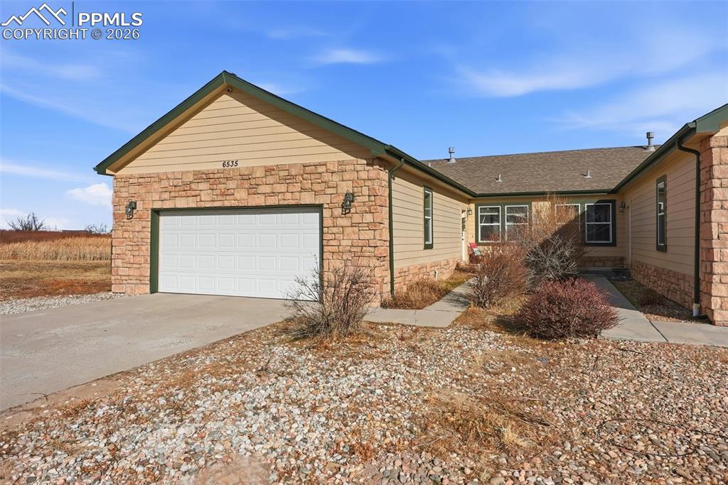 View of property exterior with stone siding, a garage, and driveway