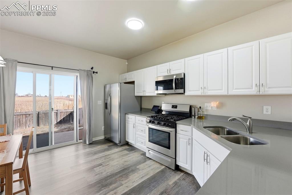 6535 Gelbvieh Road Peyton, CO 80831 - Photo 8 of 41 Kitchen featuring stainless steel appliances, white cabinets, light wood-style flooring, and light stone countertops