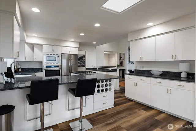 a kitchen with stainless steel appliances kitchen island granite countertop a stove top oven a sink a refrigerator with white cabinets and wooden floor