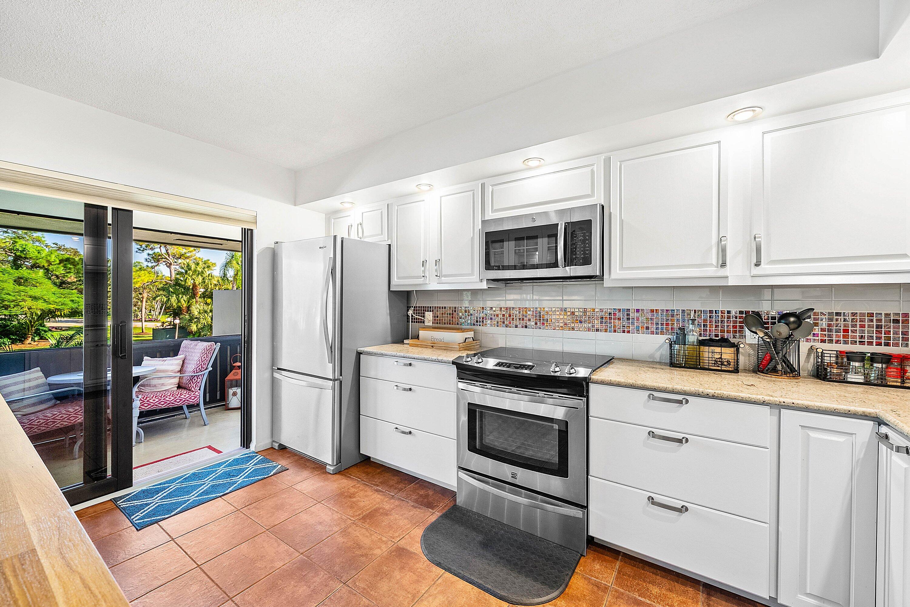 11126 Quail Covey Road, Unit MOCKINGBIRD Boynton Beach, FL 33436 - Photo 9 of 58 a kitchen with stainless steel appliances granite countertop a stove top oven a sink dishwasher a dining table and chairs with wooden floor
