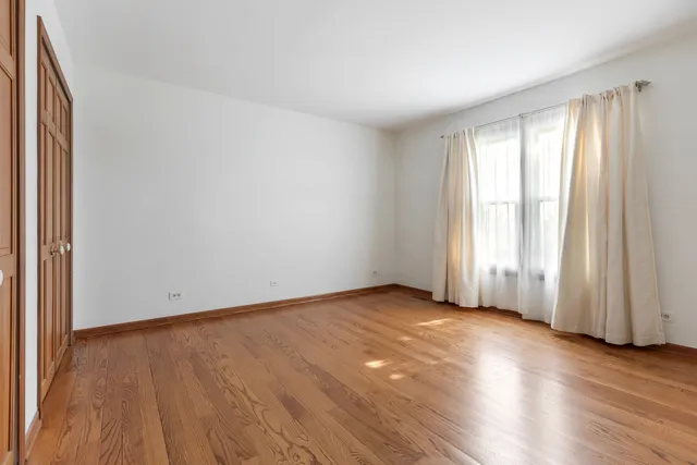 an empty room with wooden floor and windows with curtains