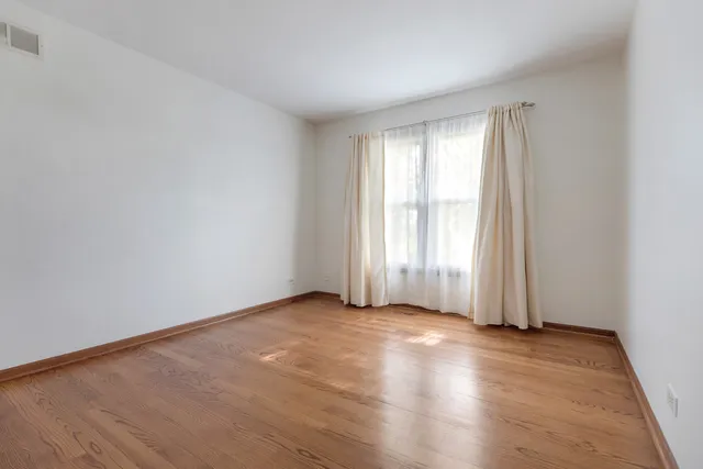 an empty room with wooden floor and windows with curtains