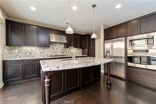 a kitchen with granite countertop wooden cabinets a counter top space stainless steel appliances and wooden floor