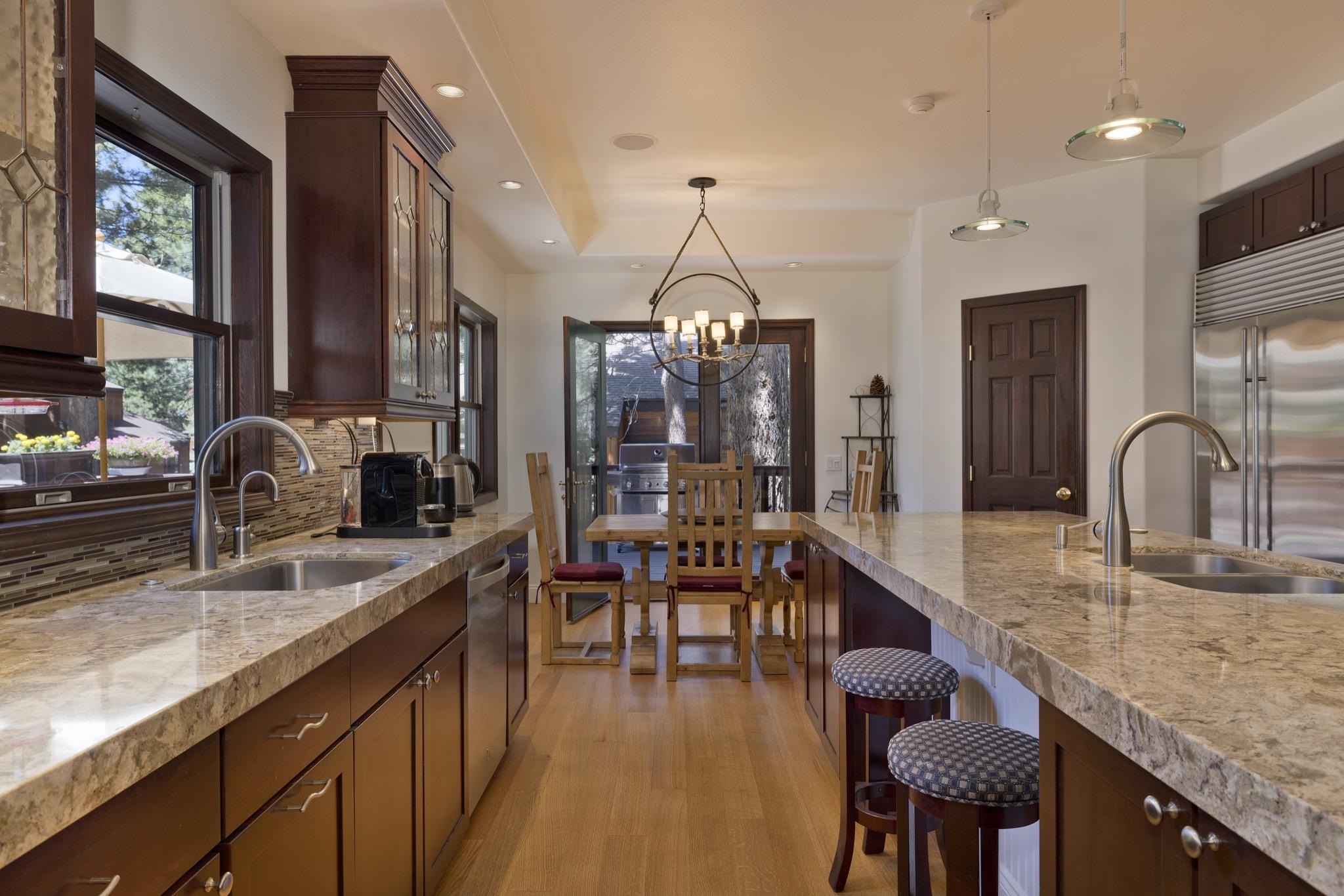 378 Ridge Way Mammoth Lakes, CA 93546 - Photo 10 of 43 Kitchen featuring wood-finish flooring, custom cabinetry with glass-front uppers, stone countertops, a tile backsplash, and stainless steel appliances