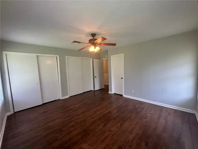 a view of an empty room with wooden floor and a ceiling fan